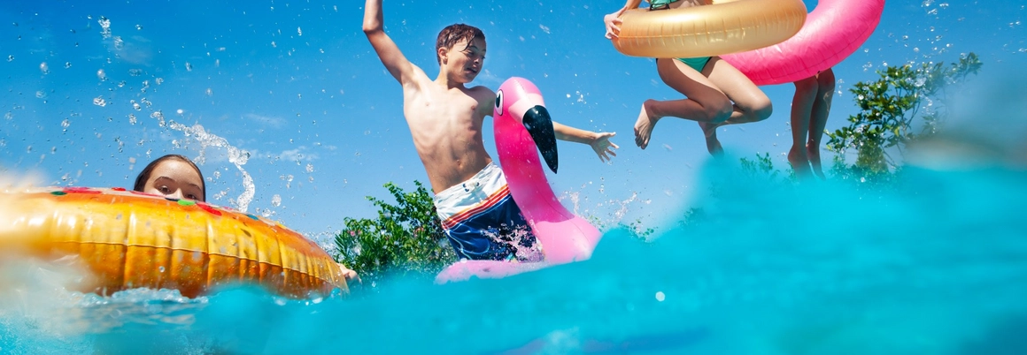 Kinder springen mit Schwimmtieren in Pool